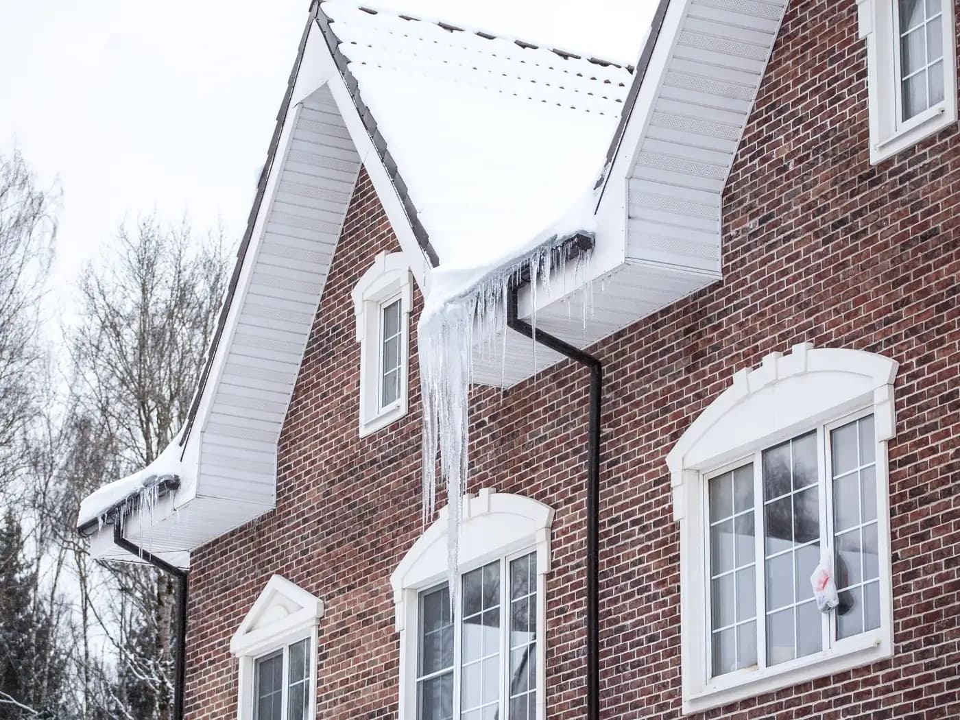 Maison de brique au toit enneigé, glaçons le long de la gouttière